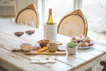 Wood table with a decorative spread of wine, charcuterie, and cupcakes.